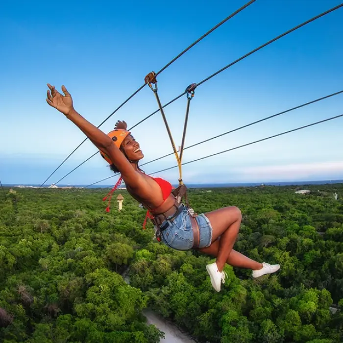 Woman ziplining with arms wide open across jungle