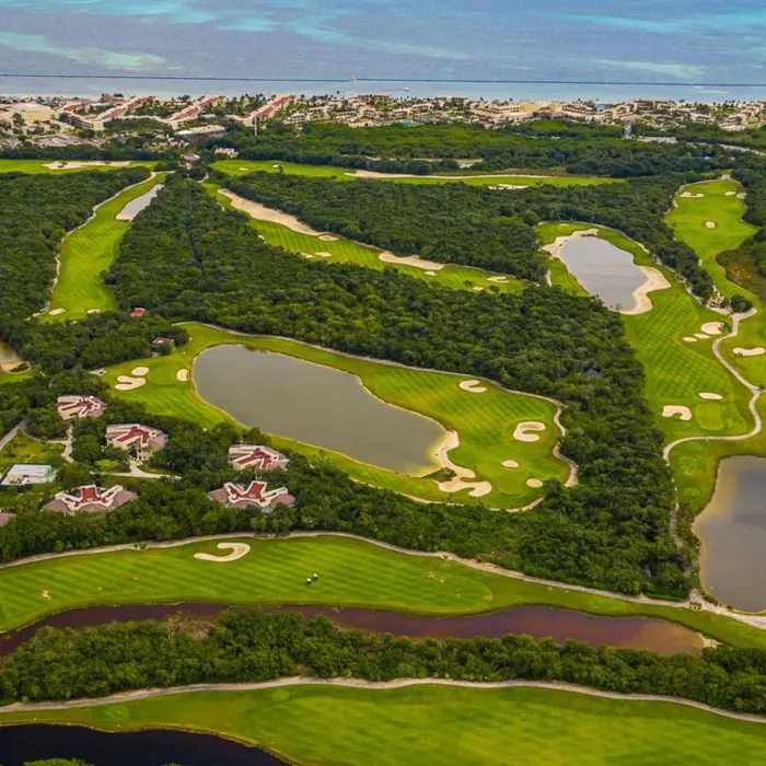 An expansive aerial view of the Moon Palace Golf Course, showcasing championship fairways winding through lush mangroves and sparkling lakes with the Caribbean Sea in the distance
