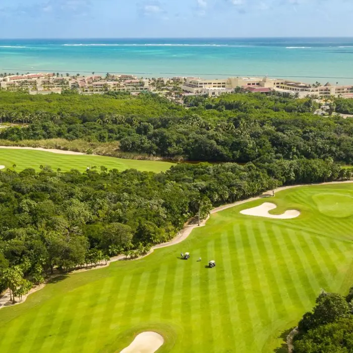 Breathtaking aerial shot of a vibrant green golf fairway carved through dense tropical jungle with the bright turquoise Caribbean Sea in the background.