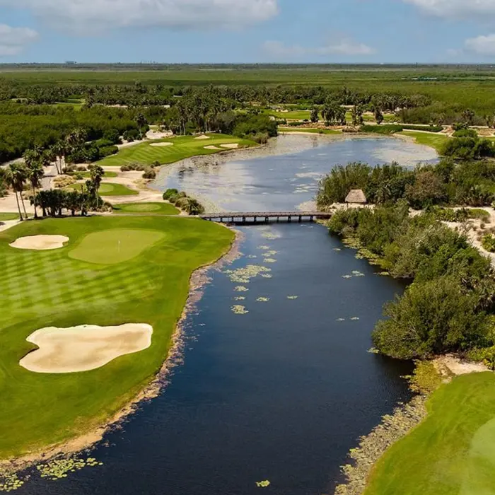 A sweeping aerial perspective of lush fairways separated by a tranquil lake and a wooden bridge at the luxury Moon Palace golf resort.