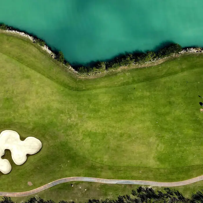 View across the water of a championship golf green with luxury waterfront homes, docked yachts, and clear blue skies in Puerto Cancún