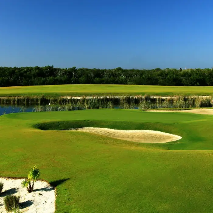 A beautifully maintained golf green protected by white sand bunkers and a tranquil lake bordered by native reeds at Moon Palace Golf Course.
