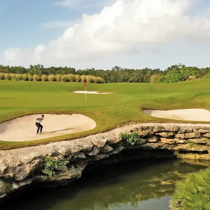 A golfer hitting a strategic shot out of a sand bunker next to a unique natural rock formation and water hazard at the championship golf course.