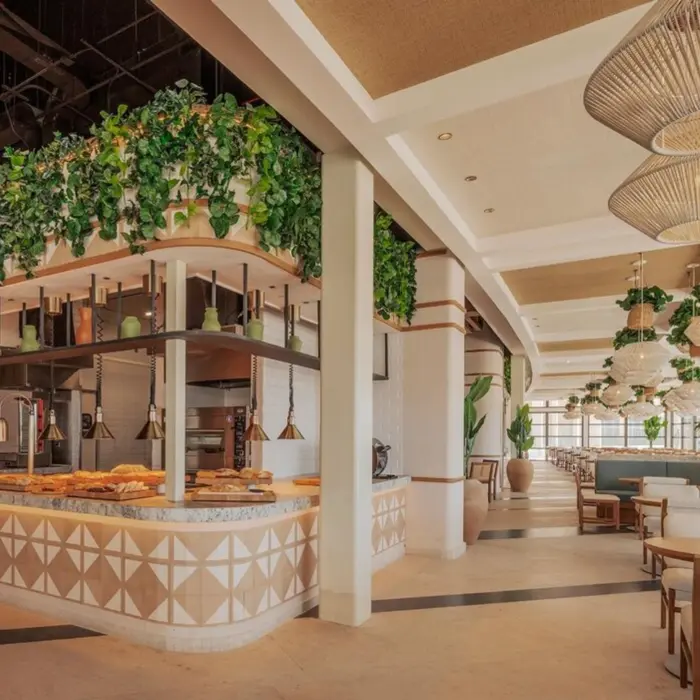 The interior of a bright and stylish restaurant at AVA Cancun with a food station and greenery.