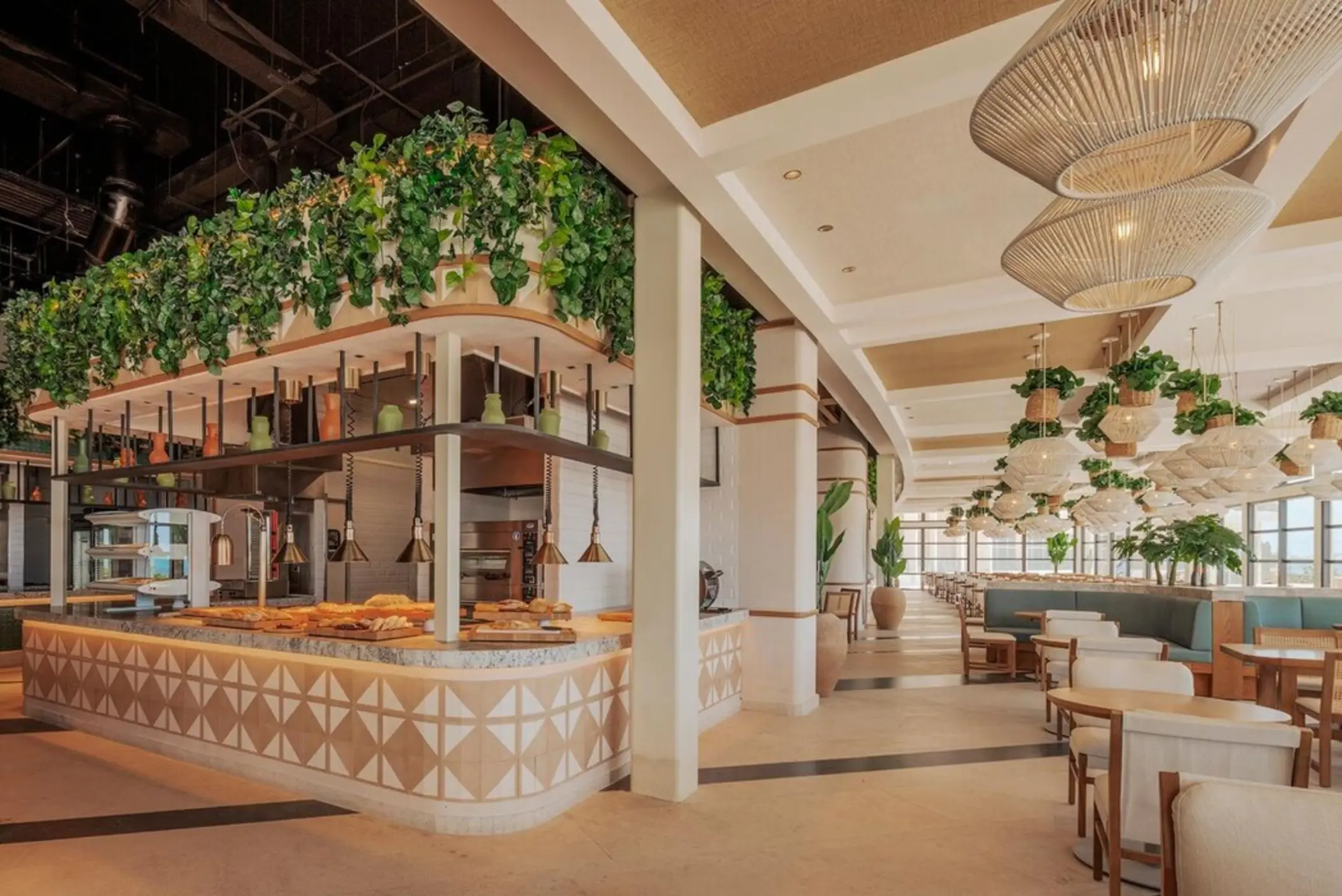 The interior of a bright and stylish restaurant at AVA Cancun with a food station and greenery.