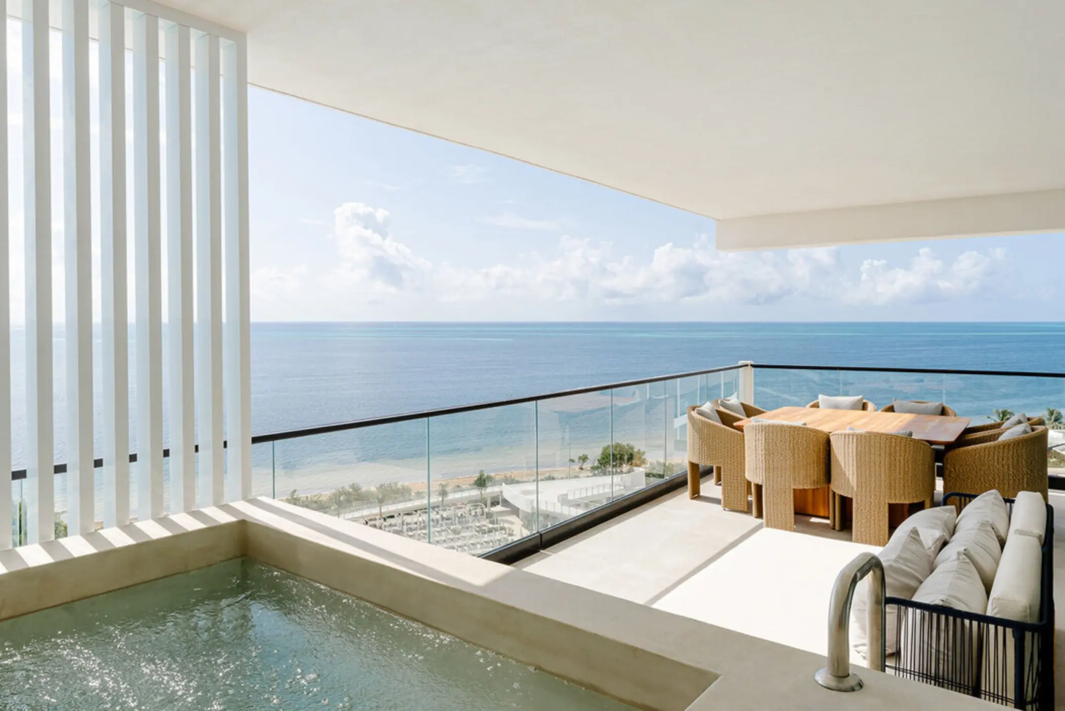 A stunning ocean view from a luxurious suite balcony with an outdoor dining set and a hot tub.