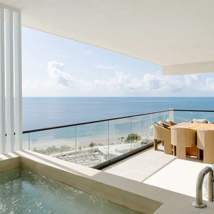 A stunning ocean view from a luxurious suite balcony with an outdoor dining set and a hot tub.