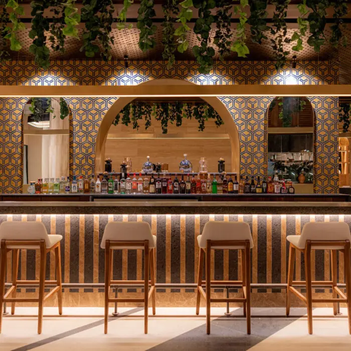 A modern bar at AVA Cancun resort featuring a geometric archway and hanging plants.