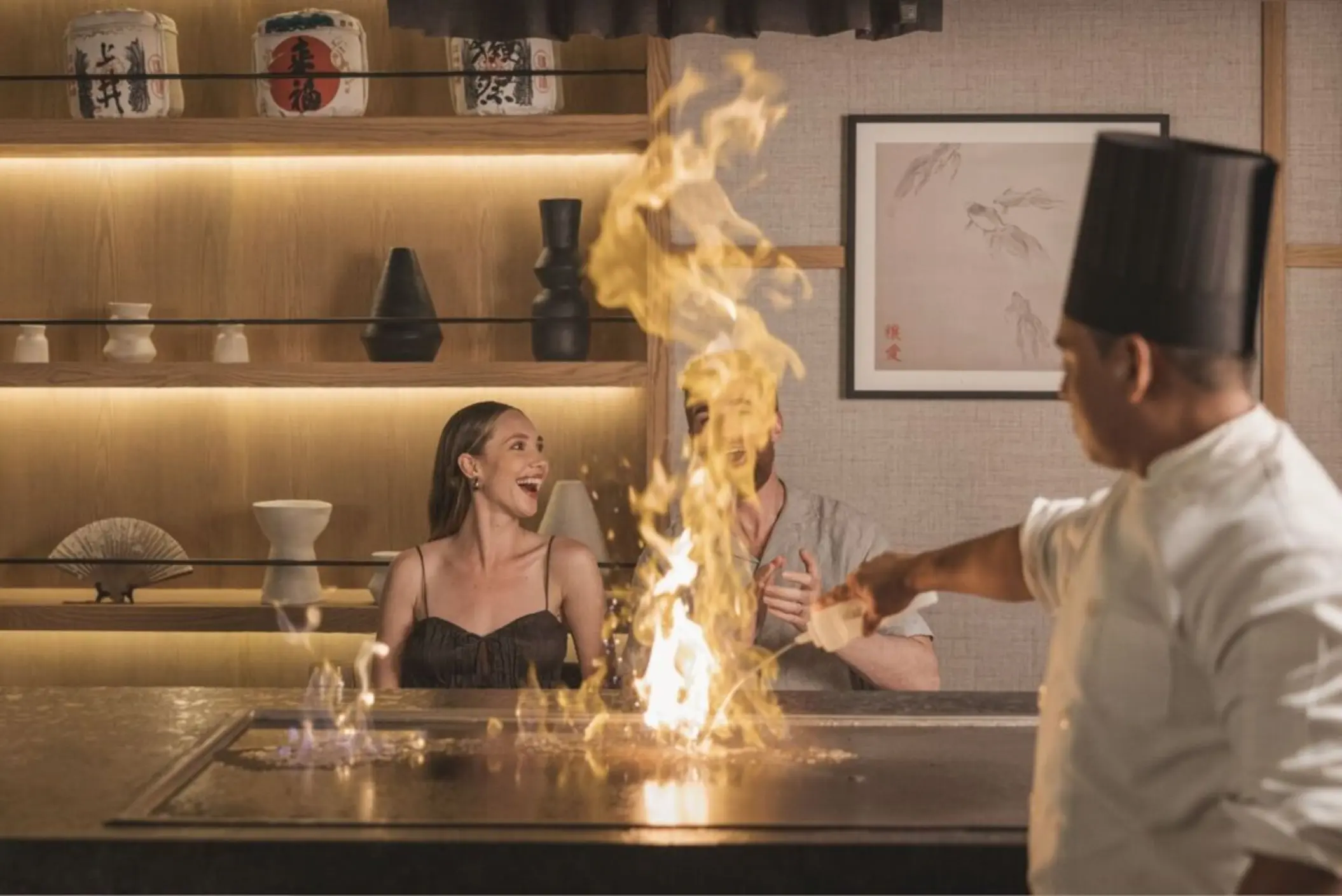 A chef preparing teppanyaki for a smiling couple at a restaurant in AVA Cancun.