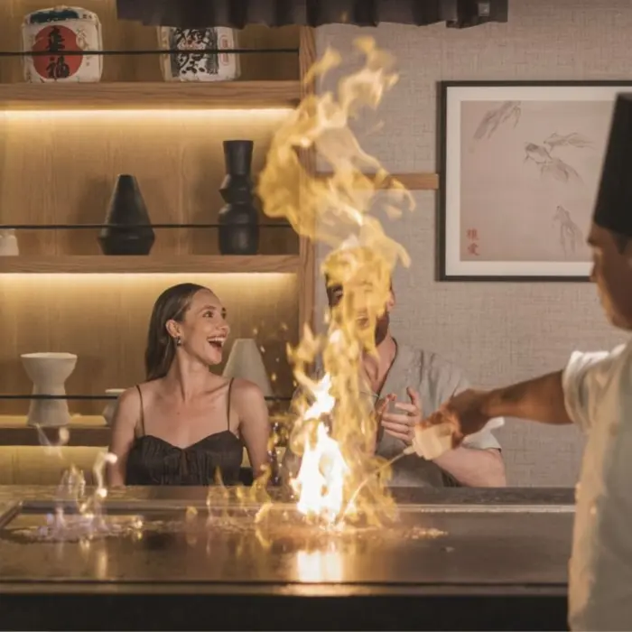 A chef preparing teppanyaki for a smiling couple at a restaurant in AVA Cancun.