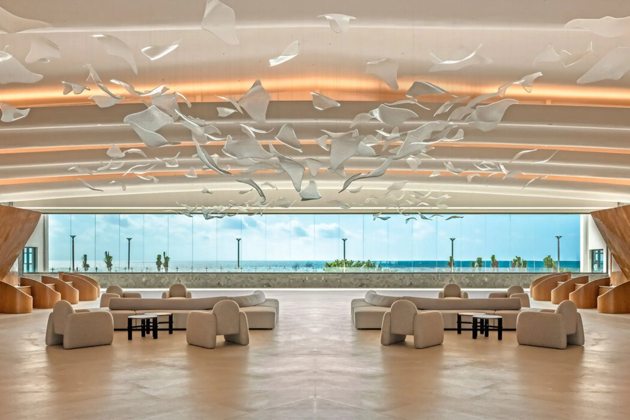 A grand, sunlit lobby with a stunning sculptural art piece and view of the ocean.