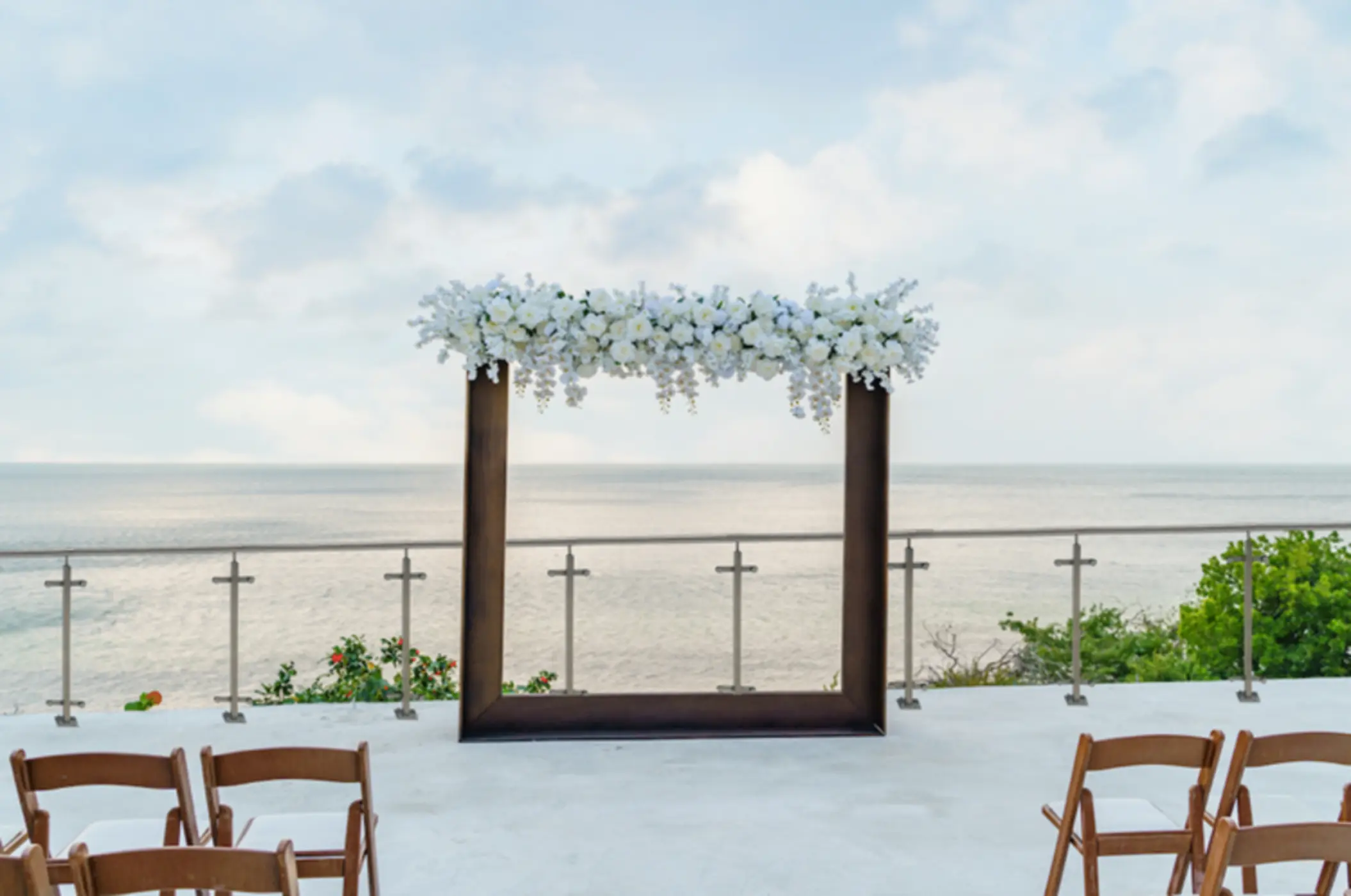 An outdoor wedding or event venue on a terrace overlooking the ocean, with a floral archway.
