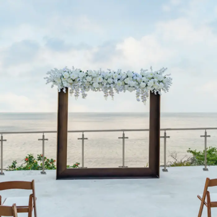 An outdoor wedding or event venue on a terrace overlooking the ocean, with a floral archway.