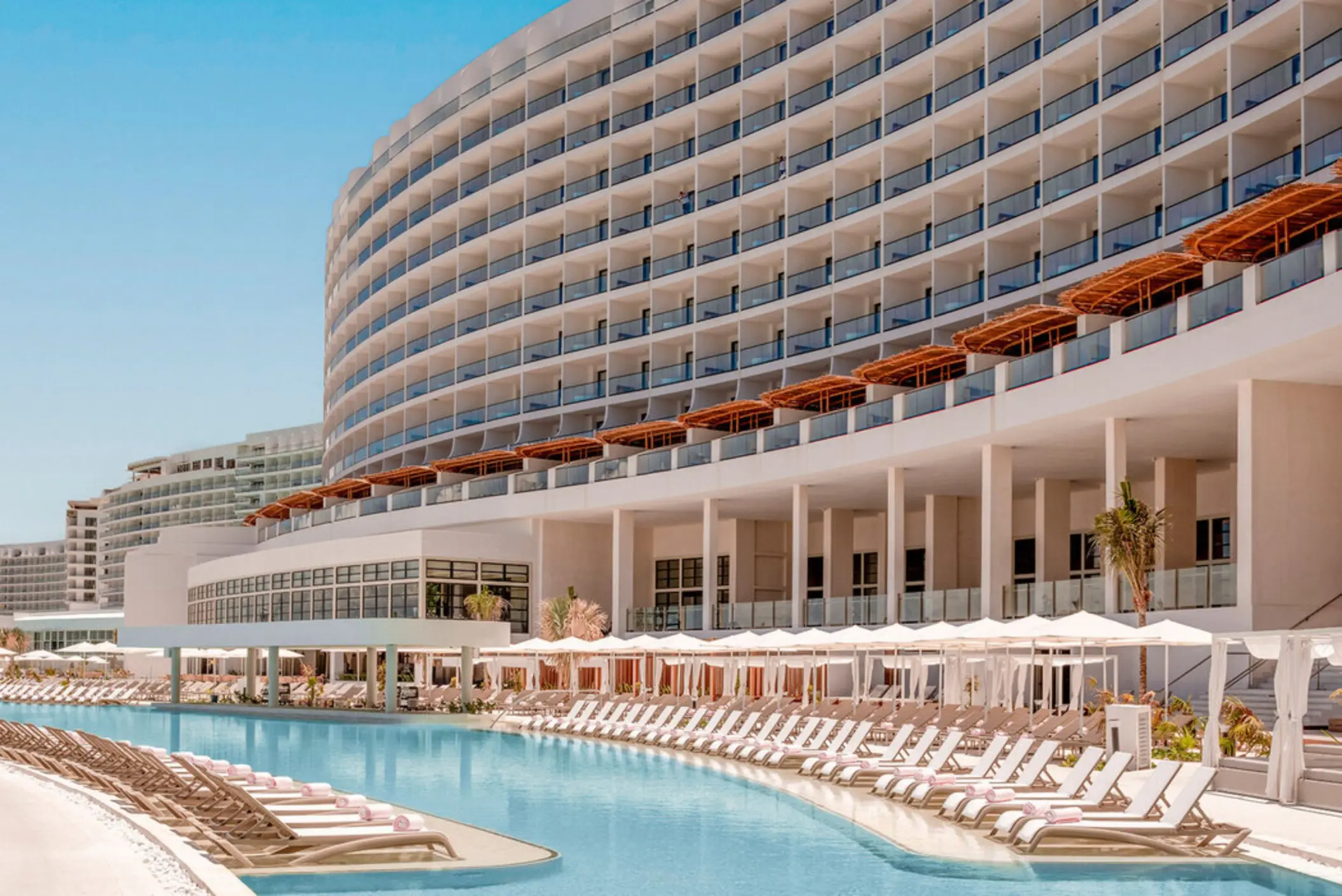 A large, luxurious resort building with a long, winding swimming pool and many lounge chairs.