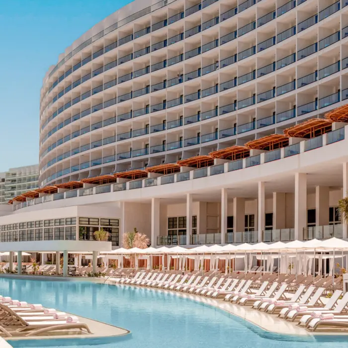 A large, luxurious resort building with a long, winding swimming pool and many lounge chairs.