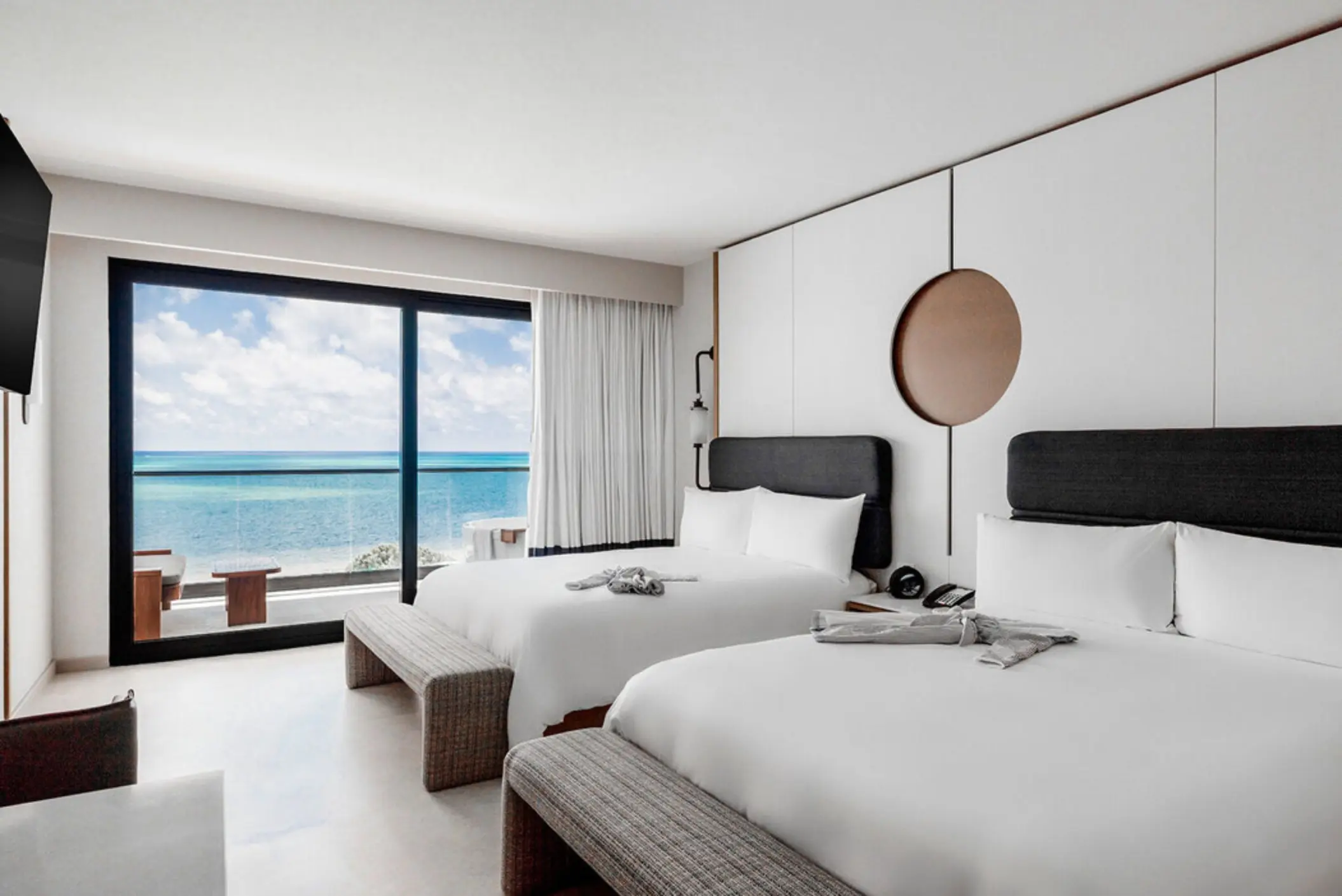 A bright hotel room with two beds, a minimalist design, and an ocean-facing balcony.