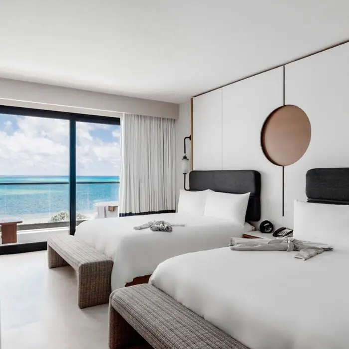 A bright hotel room with two beds, a minimalist design, and an ocean-facing balcony.