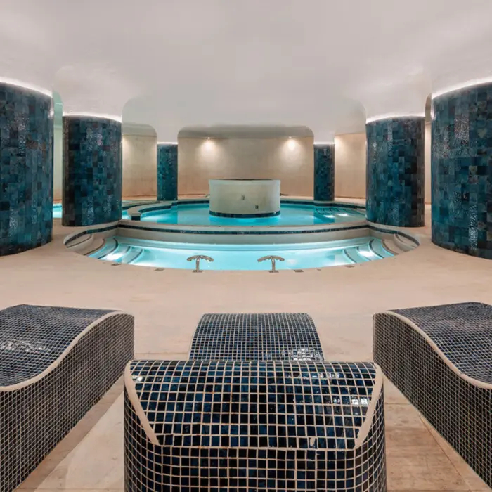 An indoor spa area with a round pool, blue tiled walls, and chaise lounges.