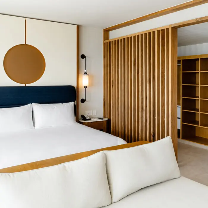 A modern hotel suite with a large bed, wooden accents, and a slatted partition.