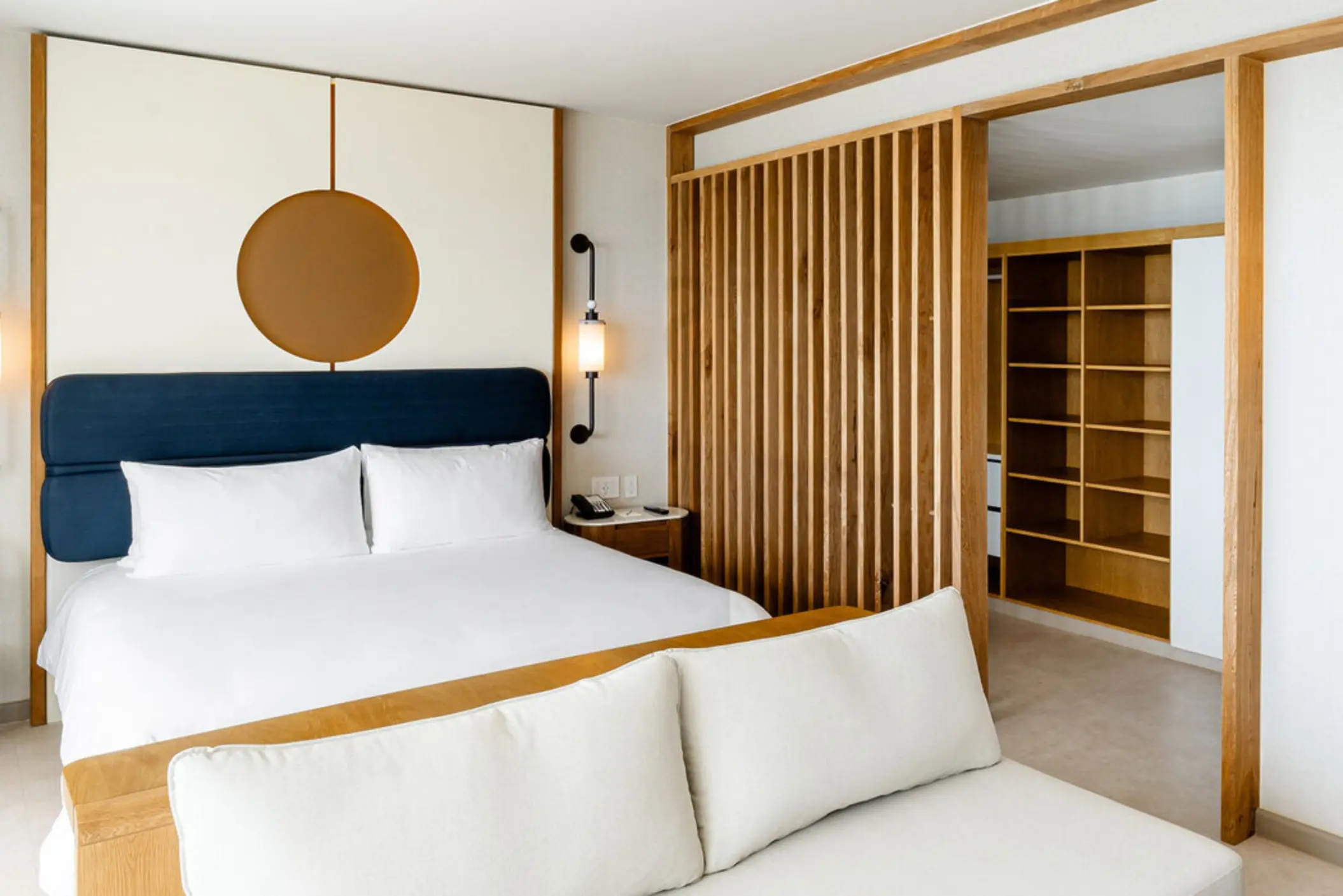 A modern hotel suite with a large bed, wooden accents, and a slatted partition.
