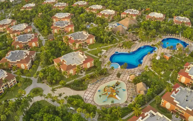 Aerial view showcasing large swimming pools surrounded by resort buildings and lush palm trees at Bahia Principe Grand Coba
