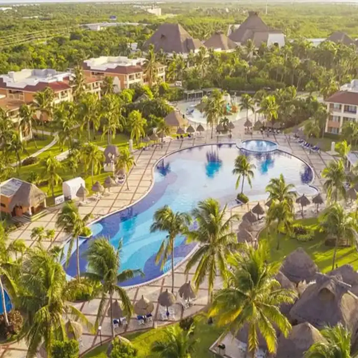 Aerial view showcasing large swimming pools surrounded by resort buildings and lush palm trees at Bahia Principe Grand Coba.
