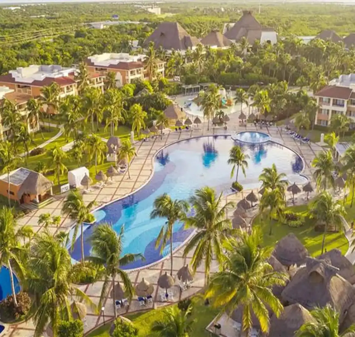 Aerial view showcasing large swimming pools surrounded by resort buildings and lush palm trees at Bahia Principe Grand Coba.