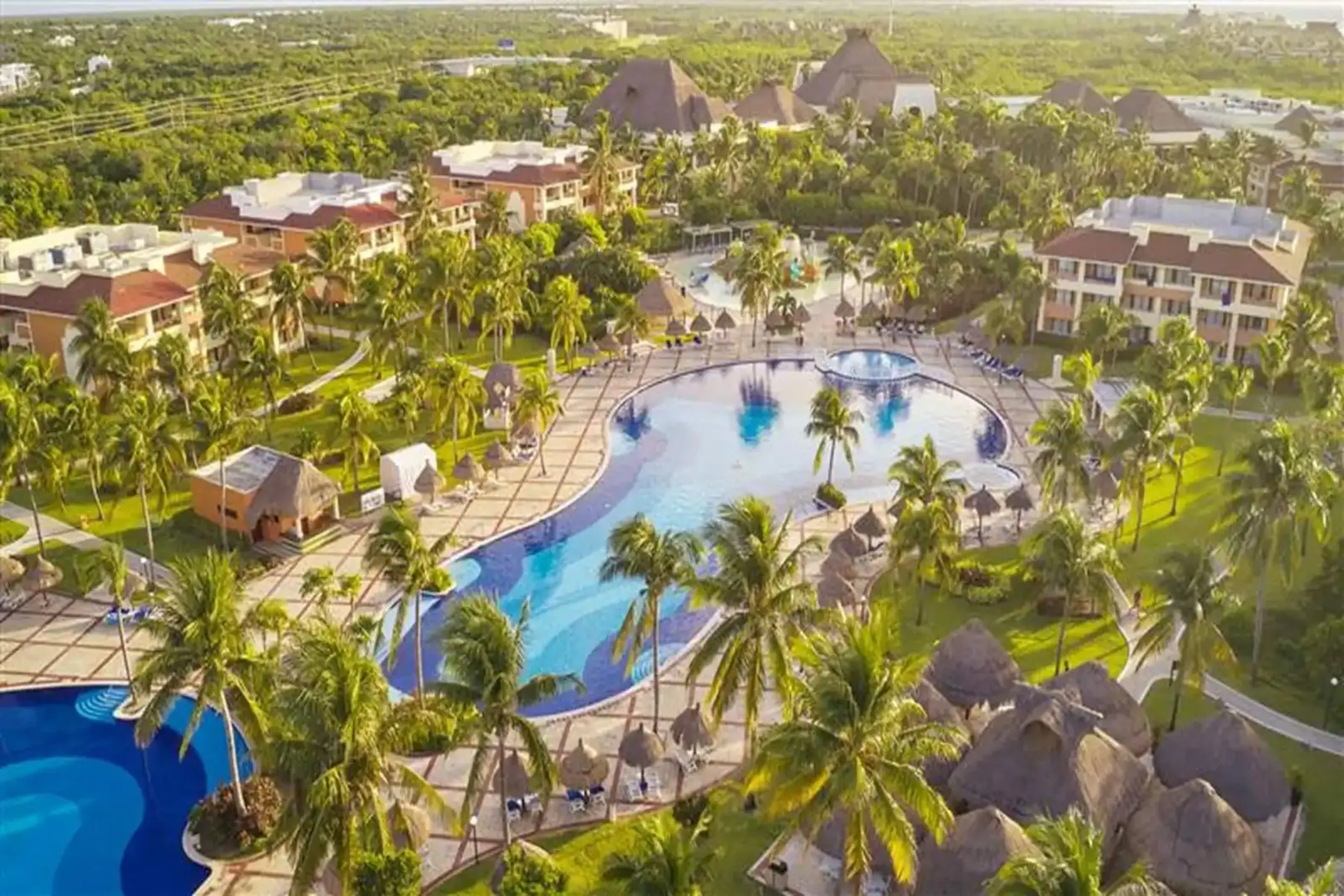 Aerial view showcasing large swimming pools surrounded by resort buildings and lush palm trees at Bahia Principe Grand Coba.
