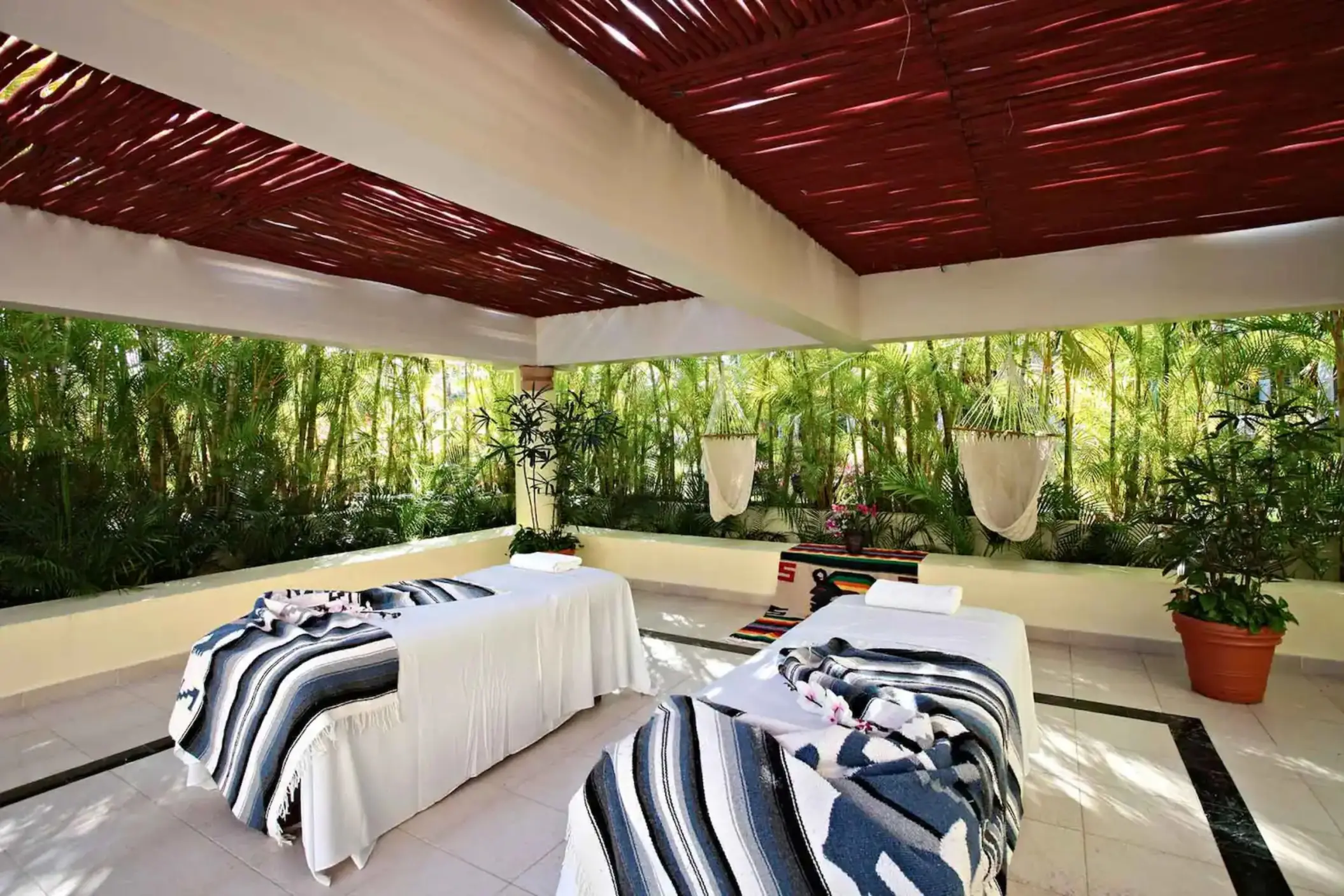 Outdoor spa area with two massage beds under a covered patio, surrounded by green foliage at Bahia Principe Grand Coba.