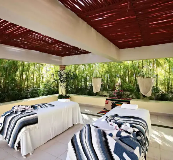 Outdoor spa area with two massage beds under a covered patio, surrounded by green foliage at Bahia Principe Grand Coba.