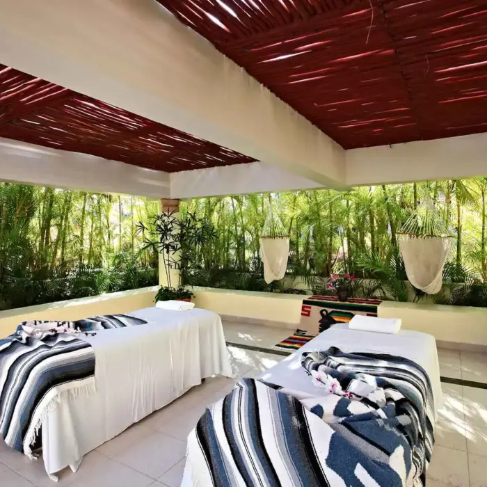 Outdoor spa area with two massage beds under a covered patio, surrounded by green foliage at Bahia Principe Grand Coba.