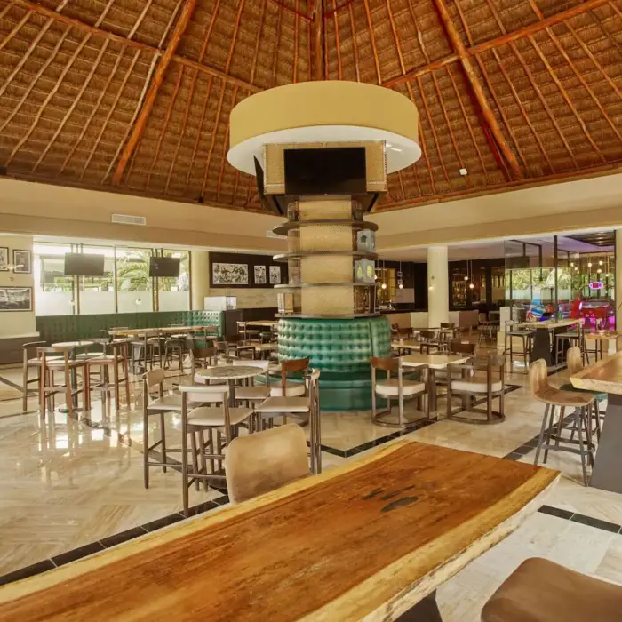Interior of a resort restaurant with various seating arrangements and a high thatched roof at Bahia Principe Grand Coba.