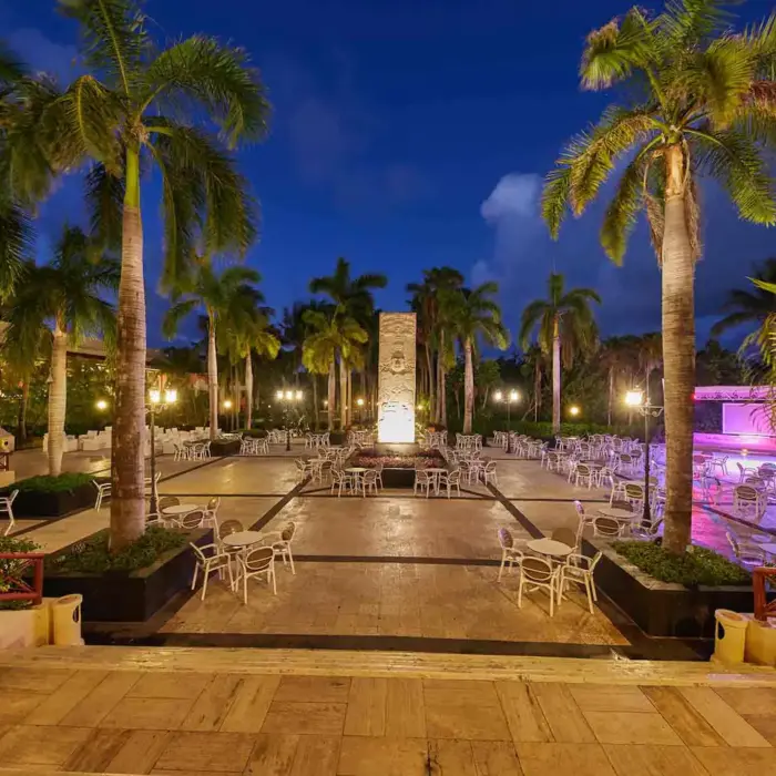 Outdoor dining area at night, illuminated by lights, with palm trees and tables set up at Bahia Principe Grand Coba.