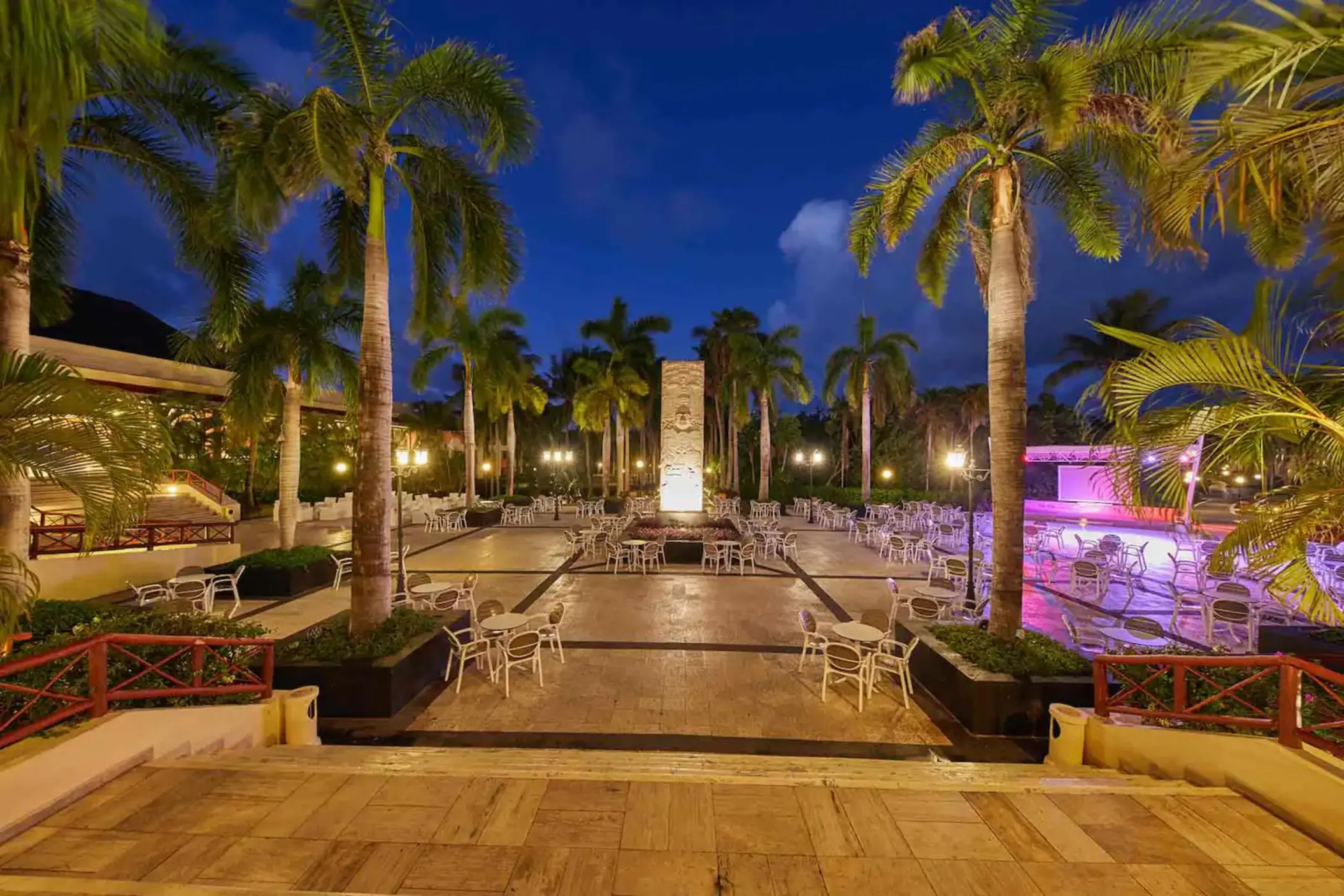 Outdoor dining area at night, illuminated by lights, with palm trees and tables set up at Bahia Principe Grand Coba.