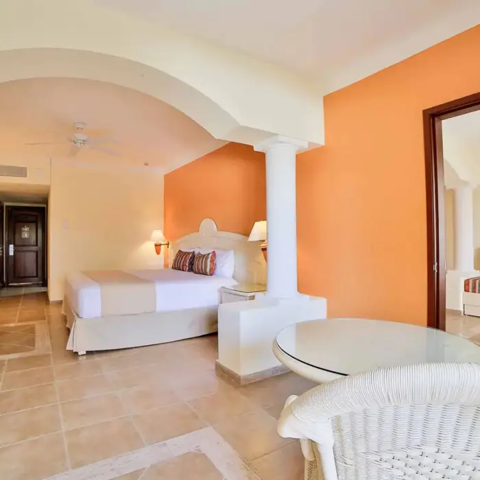 Spacious hotel suite with a king-size bed, seating area, and warm decor at Bahia Principe Grand Coba.