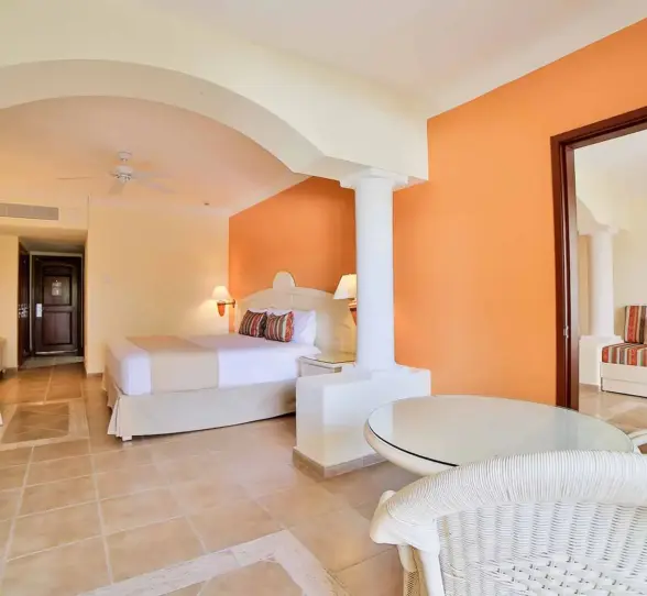 Spacious hotel suite with a king-size bed, seating area, and warm decor at Bahia Principe Grand Coba.
