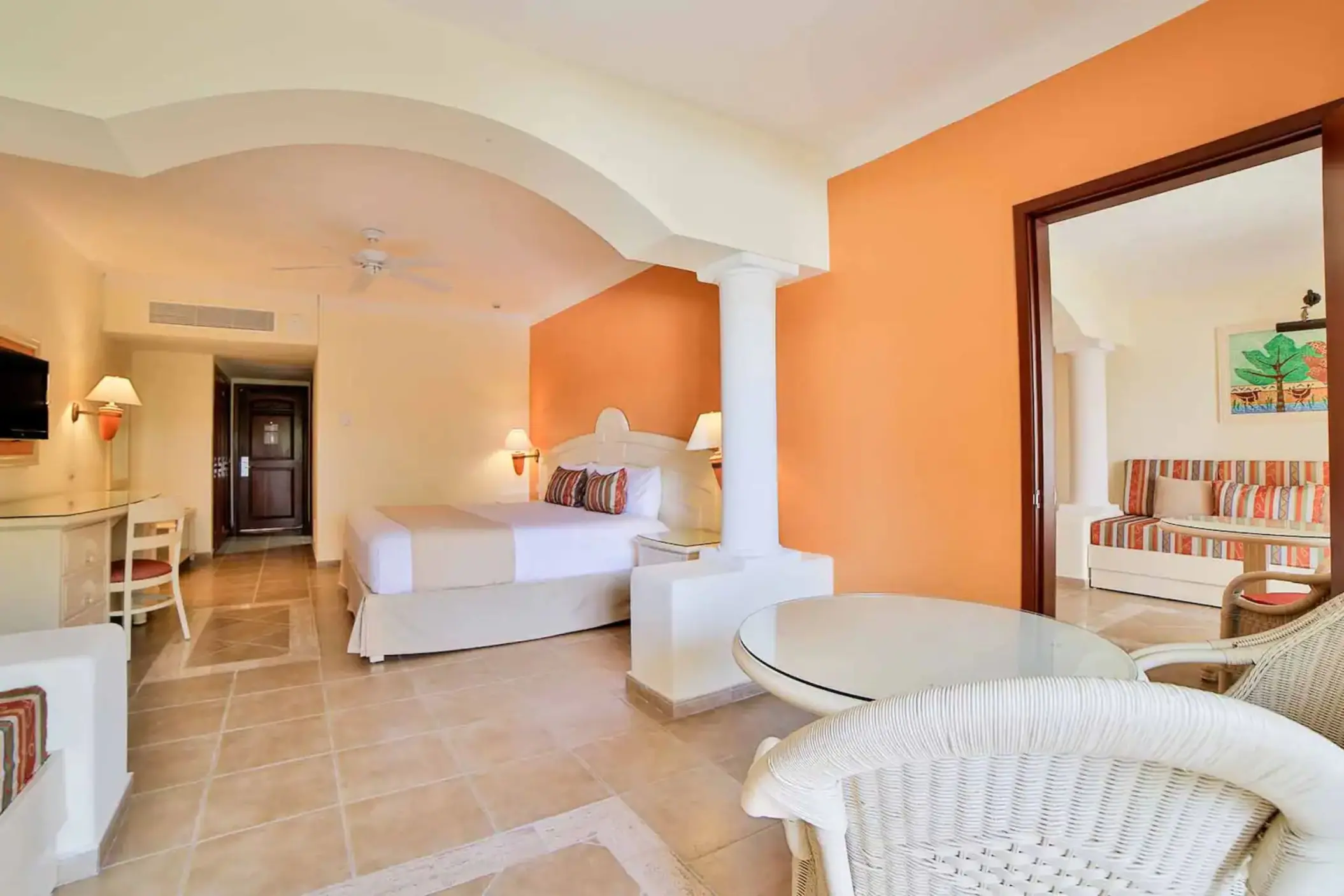 Spacious hotel suite with a king-size bed, seating area, and warm decor at Bahia Principe Grand Coba.