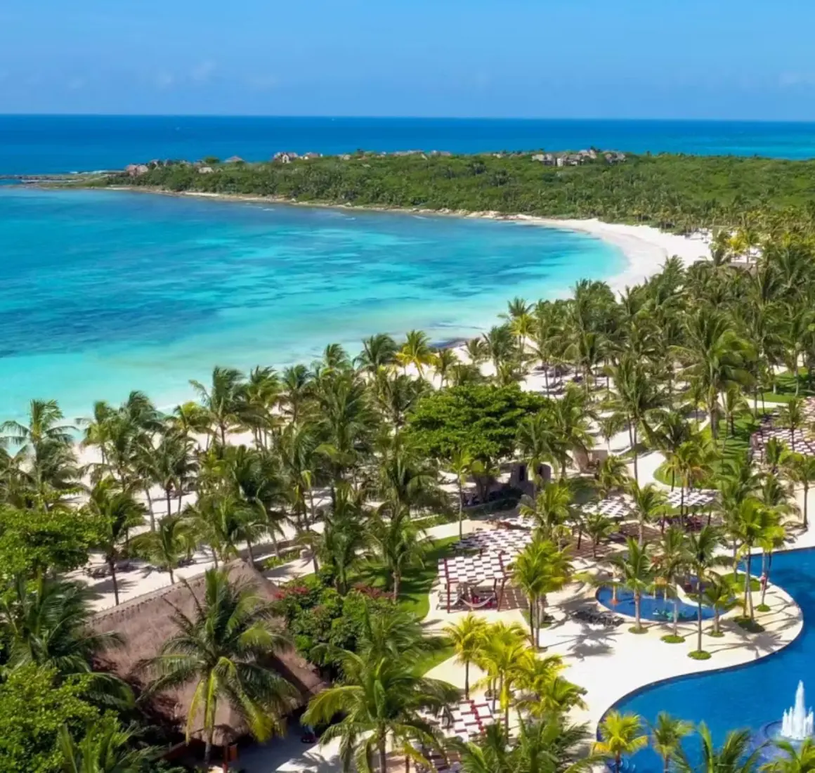 aerial view of Barceló Maya Beach resort, showcasing large pools, lush palm trees, and the expansive white sand beach bordering the turquoise ocean.