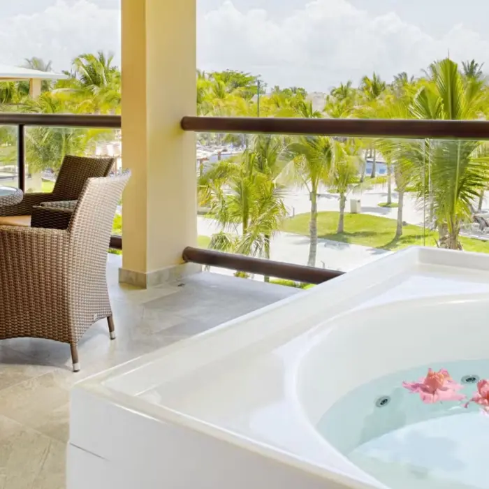 A suite balcony featuring a hot tub and a comfortable dining area with wicker chairs, overlooking the resort's lush grounds and pools.