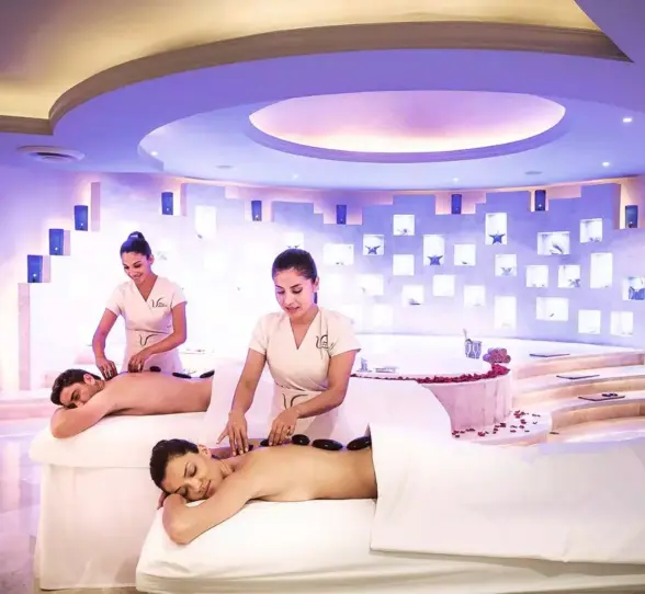 couple enjoying hot stone massages at a modern spa, with two therapists providing the treatments in a dimly lit, tranquil room with a soothing ambiance.