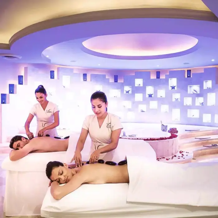couple enjoying hot stone massages at a modern spa, with two therapists providing the treatments in a dimly lit, tranquil room with a soothing ambiance.