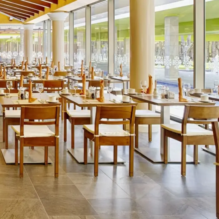 A spacious indoor dining area with many tables and chairs, large windows overlooking a pool, and a view of the resort's outdoor area.