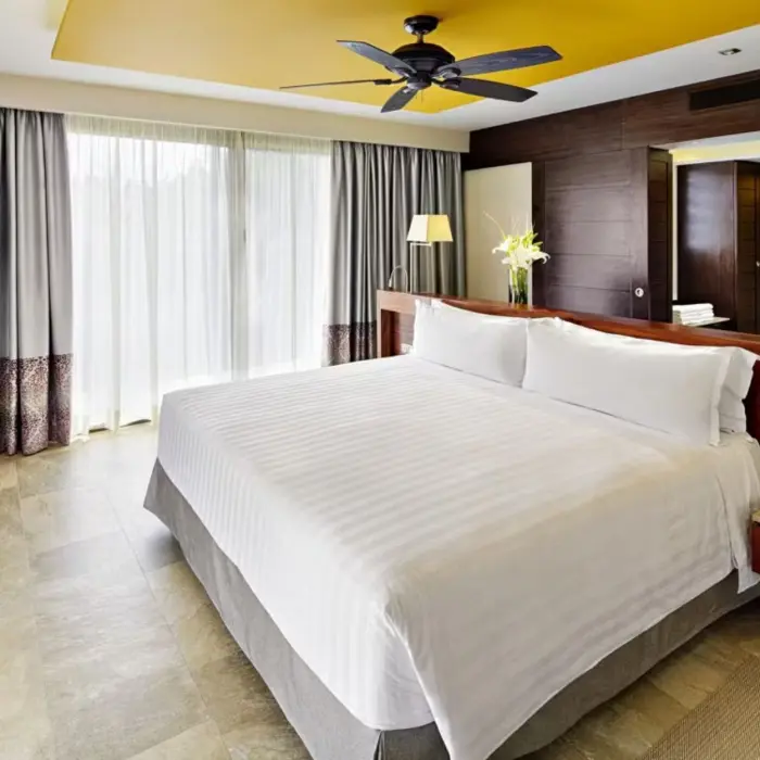 modern suite with a king-size bed, dark wood accents, contemporary lighting, a mounted television, and large windows leading to a balcony.