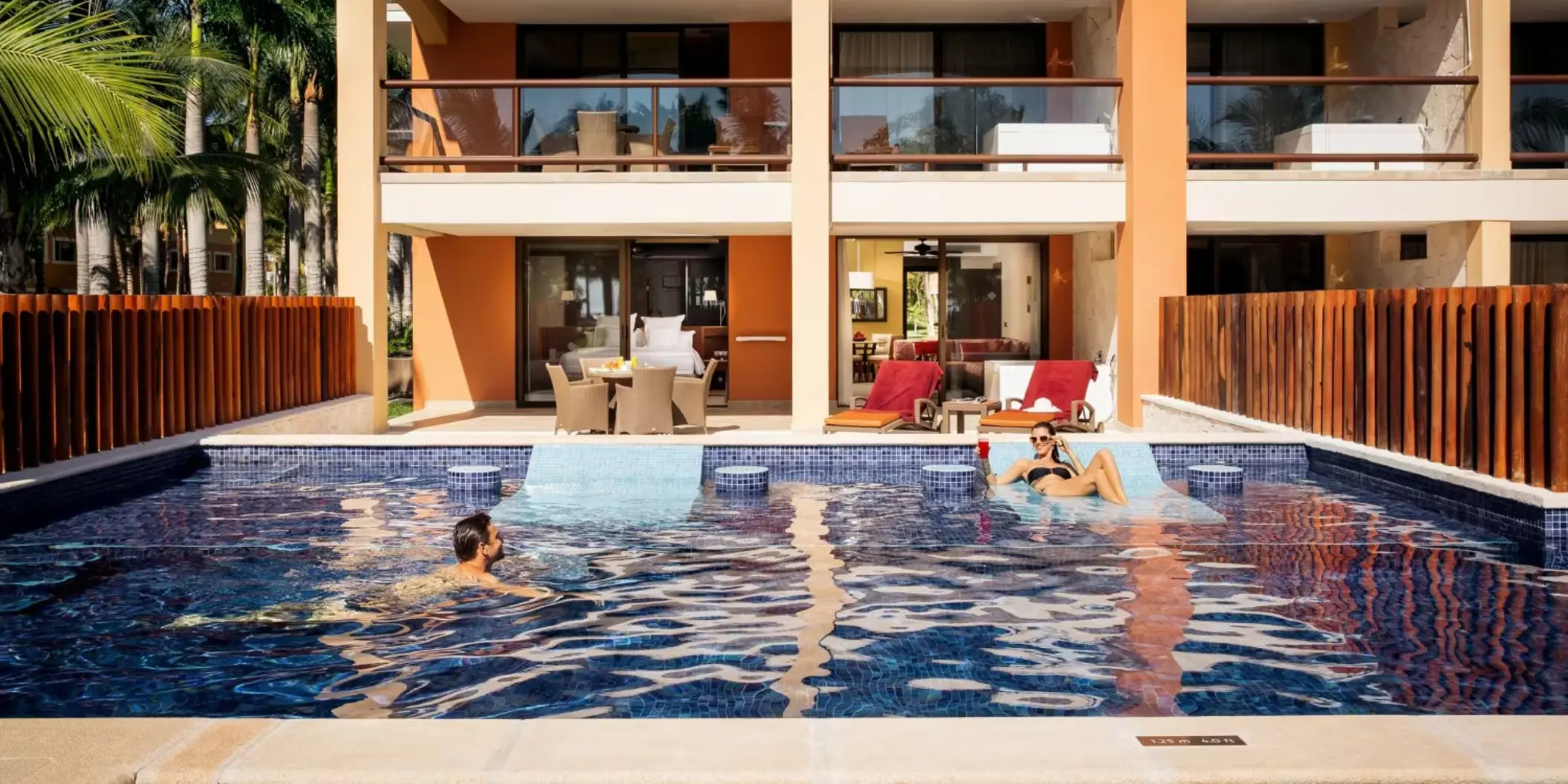 A couple relaxing in a swim-out pool directly accessible from their hotel suite balcony.