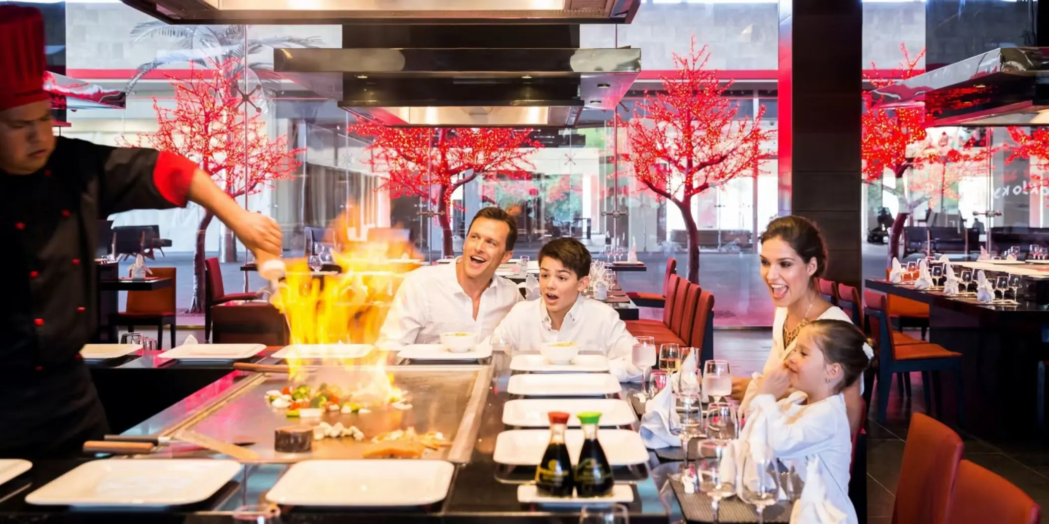 A family watching a chef prepare teppanyaki at a lively Japanese restaurant.