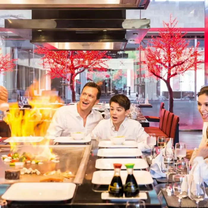 A family watching a chef prepare teppanyaki at a lively Japanese restaurant.