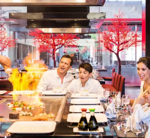 A family watching a chef prepare teppanyaki at a lively Japanese restaurant.