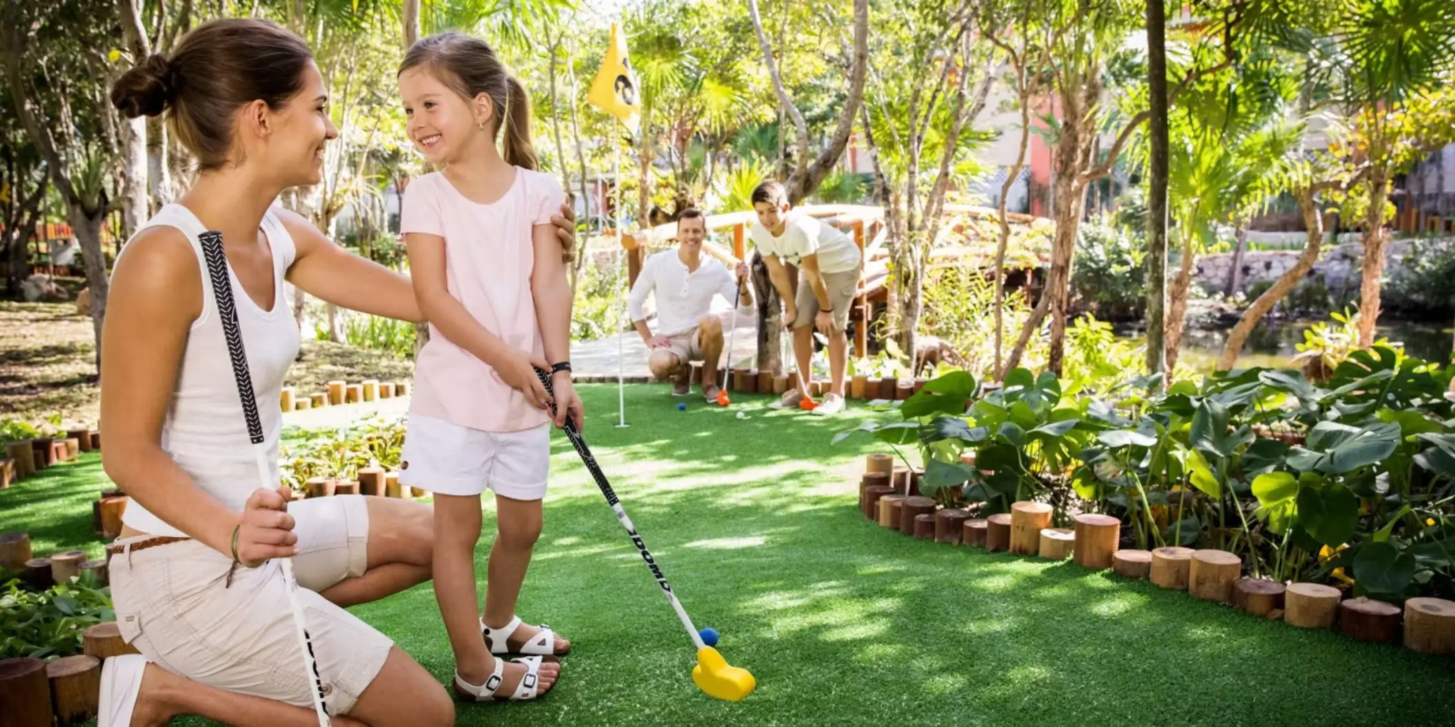 A family enjoying a game of mini-golf on a lush green course surrounded by tropical foliage.