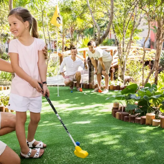 A family enjoying a game of mini-golf on a lush green course surrounded by tropical foliage.