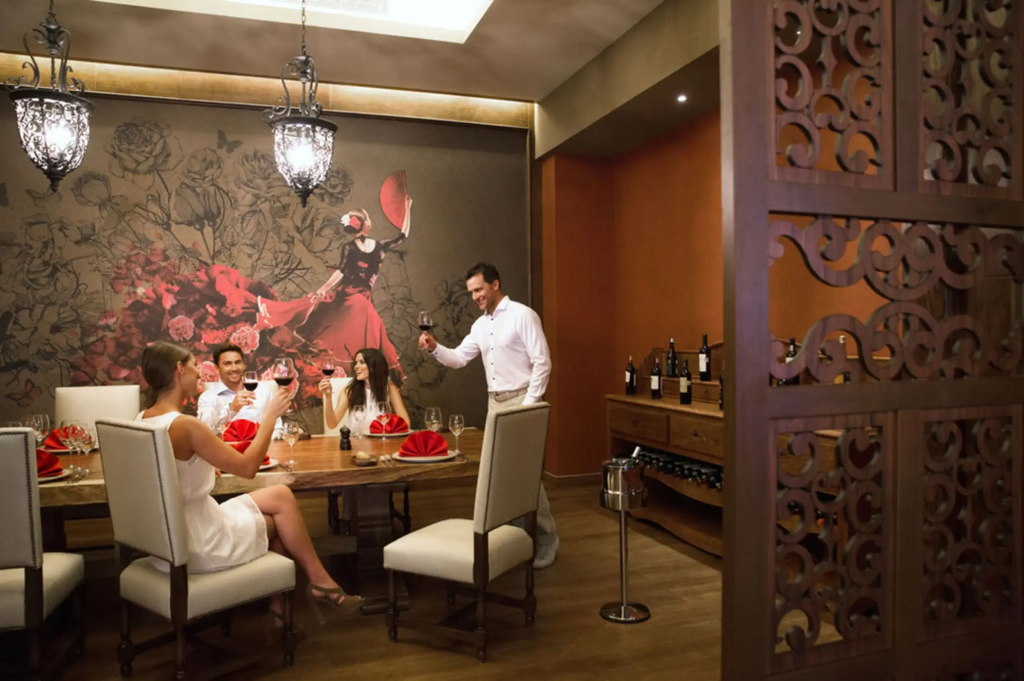 Friends enjoying wine at a stylish restaurant with ornate chandeliers and a large wall mural.